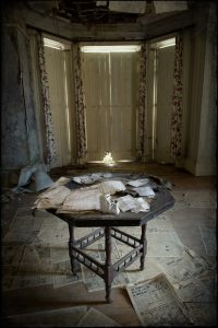 Table in room, papers on table and floor, closed shutters, derelict Manor House 'B', Norfolk, UK
