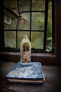 Empty bottle on a book by a window, derelict house